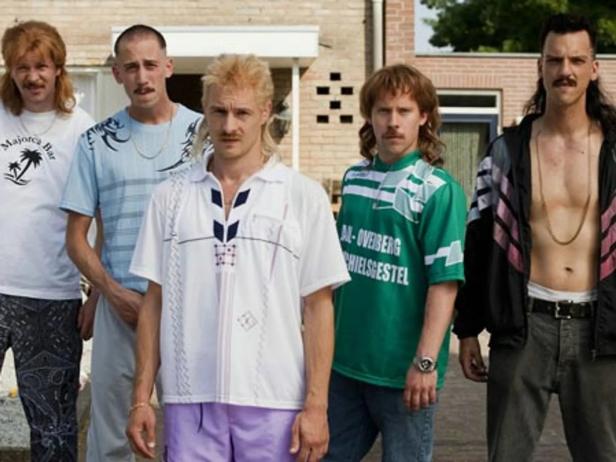 Fünf Männer mit Vokuhila-Frisuren posieren vor einem Haus.
