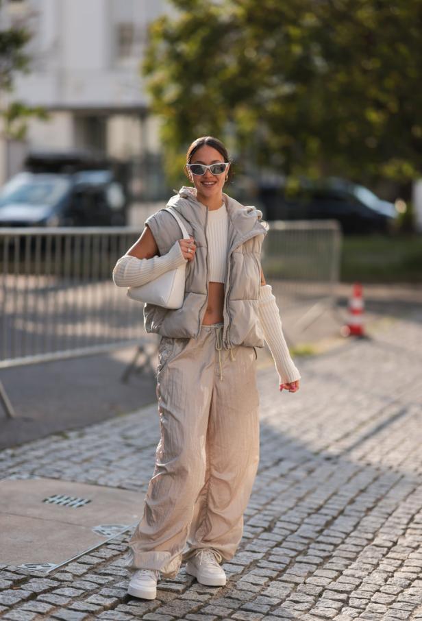 Eine Frau mit Sonnenbrille trägt eine Steppweste, weite Hose und einen Pullover mit Cut-Outs.