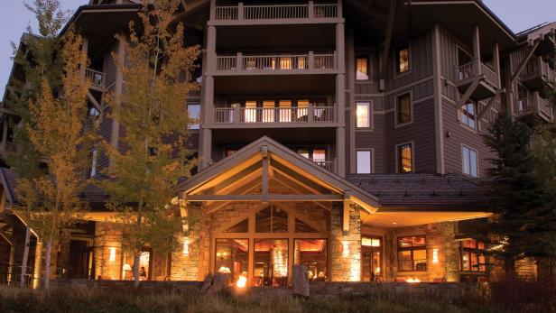 Die beleuchtete Fassade eines mehrstöckigen Hotels mit Balkonen und herbstlichen Bäumen im Vordergrund.