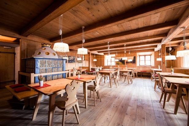 Ein traditionelles, holzvertäfeltes Restaurant mit Tischen und einem Kachelofen.