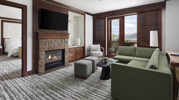 Ein Wohnzimmer mit Kamin, grünem Sofa und Blick auf die Berge.