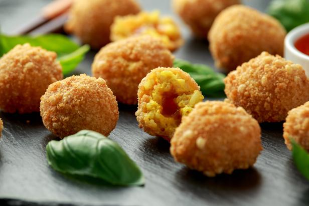 Nahaufnahme von frittierten Arancini-Reisbällchen mit Basilikumblättern.