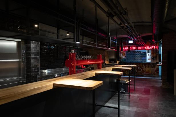 Eine Bar mit einer langen Holztheke und einer roten Bierzapfanlage.