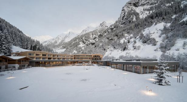 Ein modernes Hotel liegt in einer verschneiten Berglandschaft.
