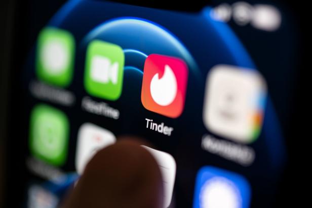 Ein Finger tippt auf dem Bildschirm eines Smartphones auf das Tinder-App-Symbol.
