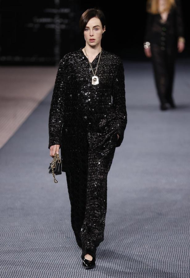 Ein Model in einem glitzernden schwarzen Hosenanzug auf einem Laufsteg.