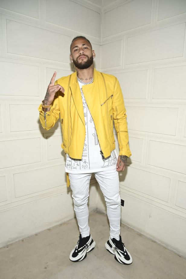 Neymar posiert in gelber Jacke, weißem Oberteil und weißen Hosen für ein Foto.