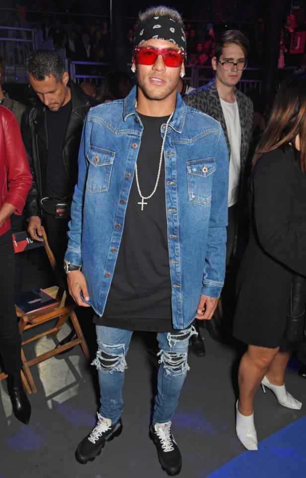 Neymar Jr. mit roter Sonnenbrille, Jeansjacke und zerrissenen Jeans bei einer Veranstaltung.