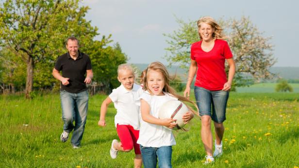 Eine Familie läuft auf einer grünen Wiese mit einem Fußball.