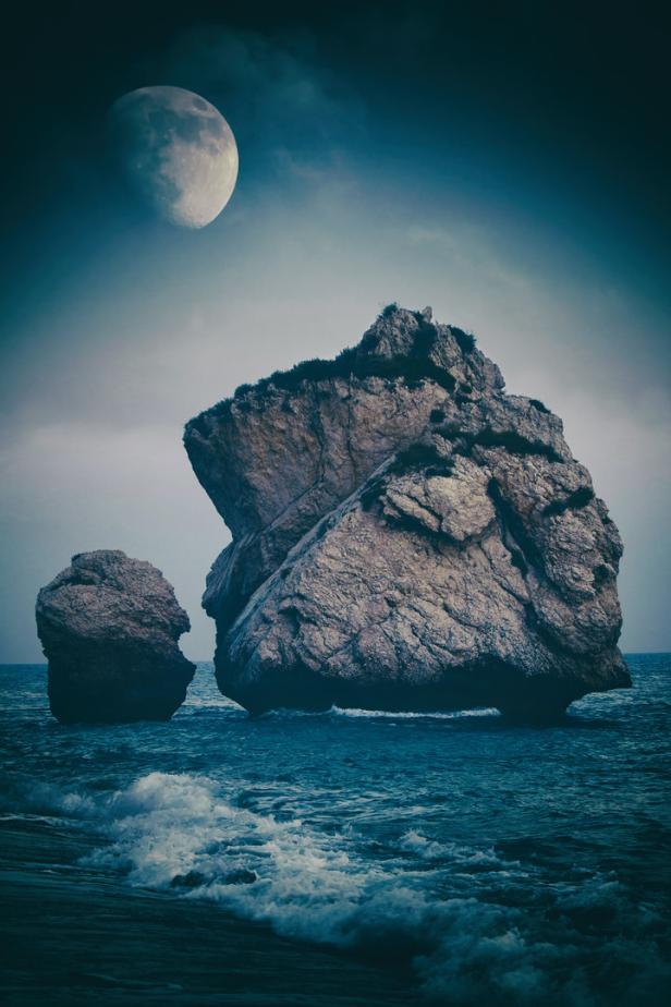Zwei Felsen ragen aus dem Meer unter einem großen Mond hervor.