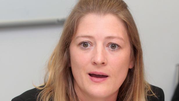 Eine Frau mit blonden Haaren und einem schwarzen Blazer spricht.