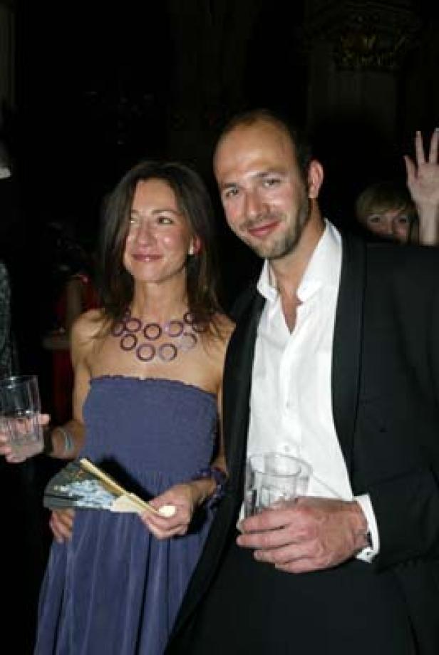 Eine Frau in einem blauen Kleid und ein Mann im Anzug halten jeweils ein Glas in der Hand.
