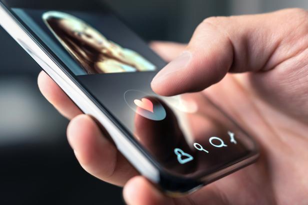 Eine Hand tippt auf einem Smartphone auf ein Herz-Symbol in einer Dating-App.