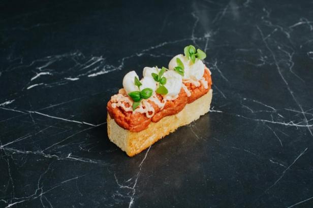 Ein belegtes Brot mit Tatar, Mozzarella und Basilikum auf einem Marmortisch.
