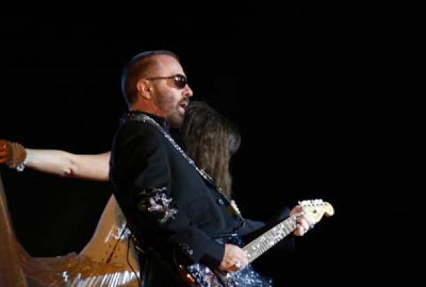 Ein Mann mit Sonnenbrille spielt Gitarre auf einer Bühne.