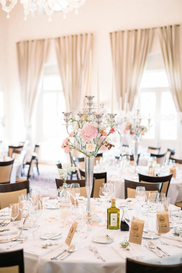 Ein festlich gedeckter Tisch mit Blumenarrangements und Kerzenleuchtern in einem eleganten Raum.