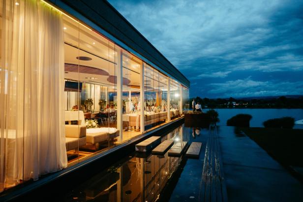 Ein modernes Restaurant mit großen Glasfenstern am Wasser bei Dämmerung.