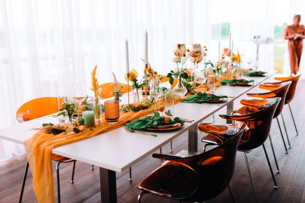 Ein festlich gedeckter Tisch mit Blumen, Kerzen und orangefarbenen Akzenten für eine Feier.