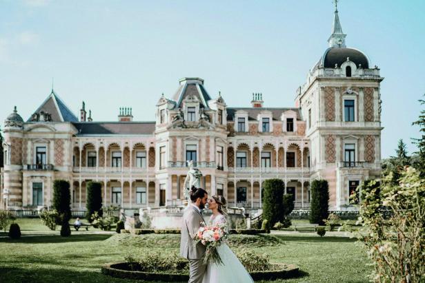 Ein Brautpaar steht vor einem Schlossgarten mit großem Schloss.