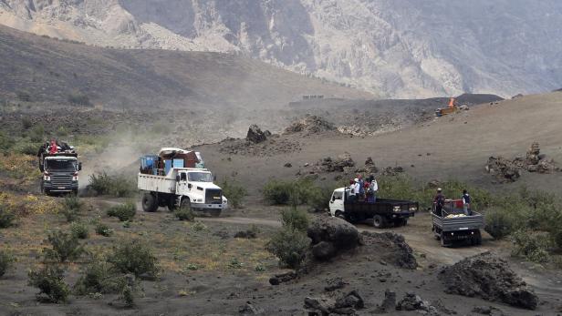 Mehrere mit Gütern und Personen beladene Lastwagen fahren durch eine vulkanische Landschaft.