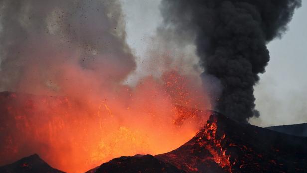 Ein Vulkan bricht aus und speit Lava und dunkle Asche in den Himmel.