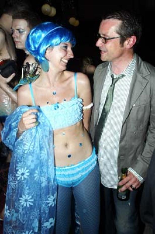 Eine Frau mit blauer Perücke und blauem Outfit unterhält sich mit einem Mann.