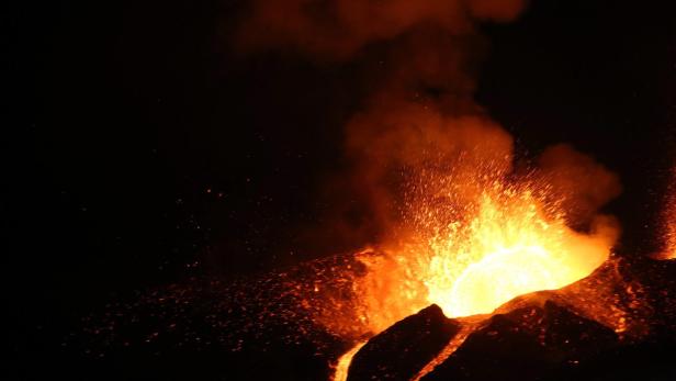 Ein Vulkan bricht nachts aus und speit Lava und Asche.
