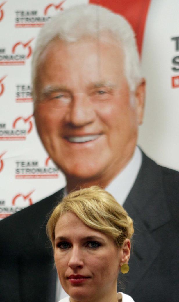 Eine Frau steht vor einem großen Porträt von Frank Stronach.