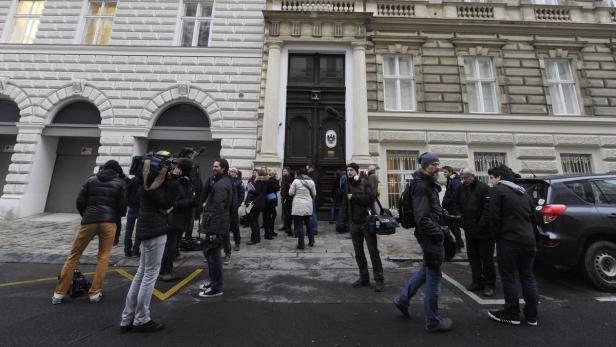 Vor einem Gebäude mit der österreichischen Flagge warten Kamerateams und Journalisten.