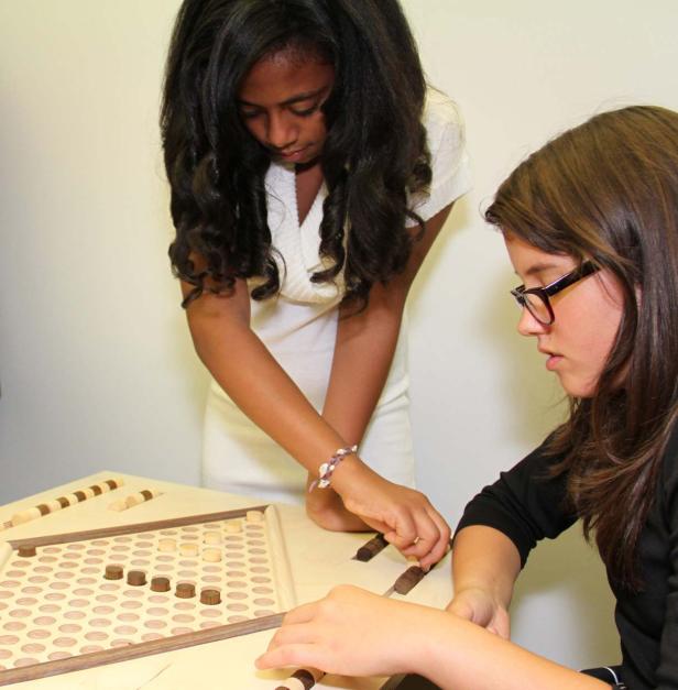 Zwei Mädchen spielen ein Brettspiel mit Holzfiguren.