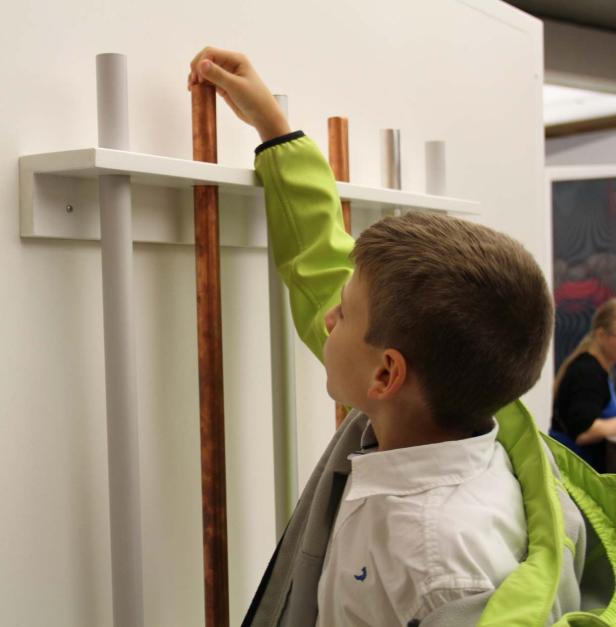 Ein Junge untersucht eine Installation mit verschiedenfarbigen Röhren.