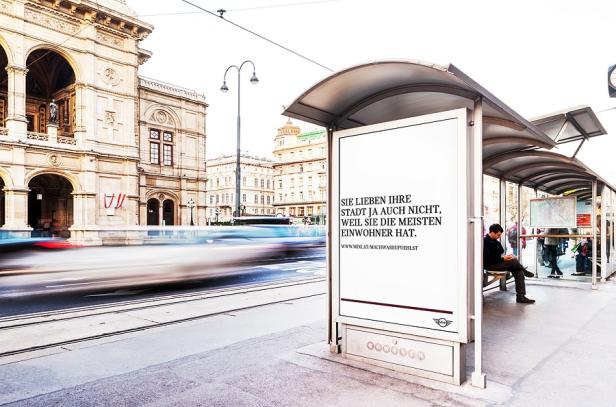 Eine Bushaltestelle in Wien mit einem Werbeplakat und der Wiener Staatsoper im Hintergrund.