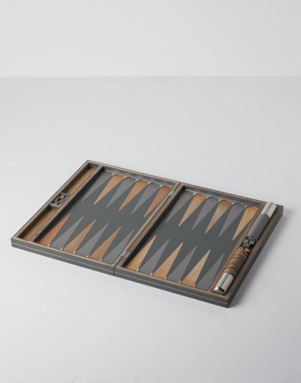 Ein geöffnetes Backgammon-Spielbrett mit grauen und hellbraunen Dreiecken liegt auf einem Tisch.