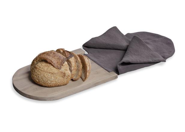 Ein Laib Brot und einige Scheiben liegen auf einem Holzbrett neben einer grauen Stoffserviette.