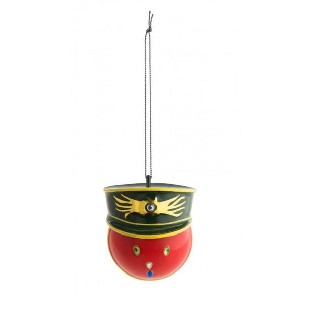 Ein roter Weihnachtsschmuck in Form eines Gesichtes mit einer grünen Militärmütze hängt an einer Schnur.