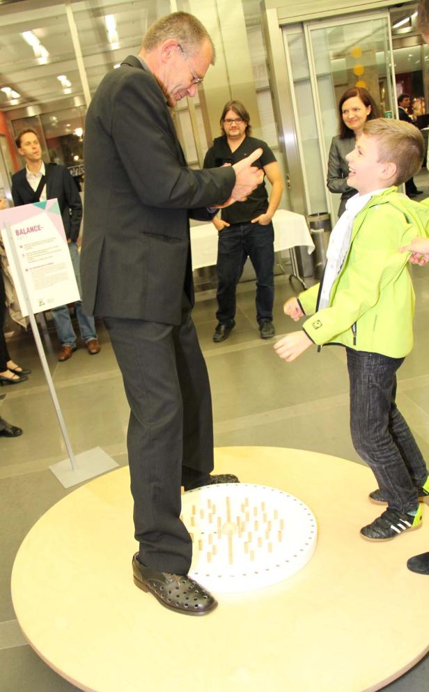 Ein Mann im Anzug balanciert auf einer Drehscheibe mit einem Jungen.