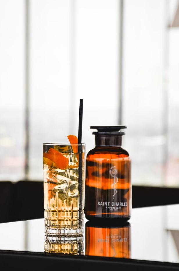 Ein Cocktail mit Eis und Orangenschale neben einer Flasche Saint Charles Apothecary.