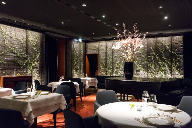 Ein elegant gedeckter Tisch in einem gehobenen Restaurant mit Pianoforte und Blumenschmuck.