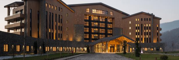 Ein großes, modernes Hotel mit Holzfassade und vielen Fenstern bei Dämmerung.
