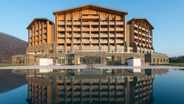 Ein großes Hotel mit Holzfassade spiegelt sich in einem ruhigen Gewässer.