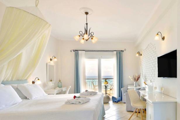 Ein helles Hotelzimmer mit Himmelbett und Blick auf das Meer.