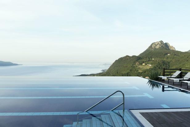 Ein Infinity-Pool mit Blick auf einen See und bewaldete Hügel.