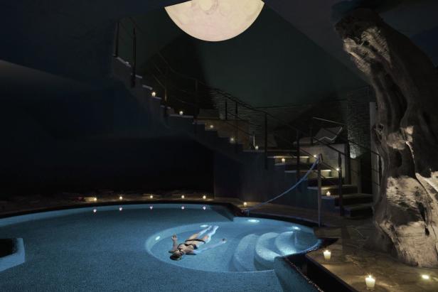 Eine Frau entspannt in einem beleuchteten Pool unter einem dekorativen Mond.