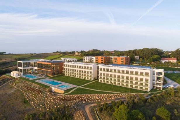 Ein modernes Hotelresort mit mehreren Gebäuden und Pools in einer grünen Landschaft.