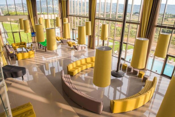 Ein weitläufiger, moderner Hotellobby-Bereich mit gelben Akzenten und großen Fenstern.