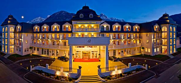 Das Grandhotel Lienz erstrahlt nachts vor einer Bergkulisse.
