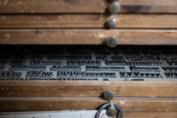 Ein Setzkasten mit alten Druckbuchstaben aus Metall in einer Holzschublade.