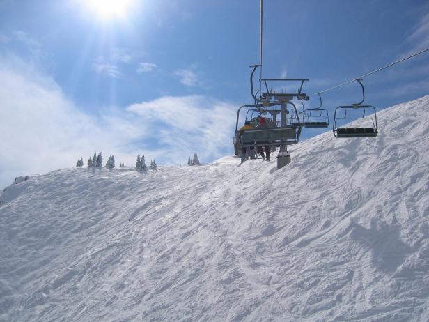 Ein Sessellift transportiert Skifahrer einen schneebedeckten Hang hinauf.