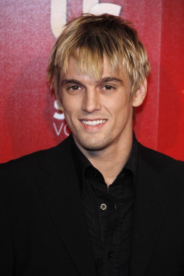 Aaron Carter lächelt vor einem roten Hintergrund.