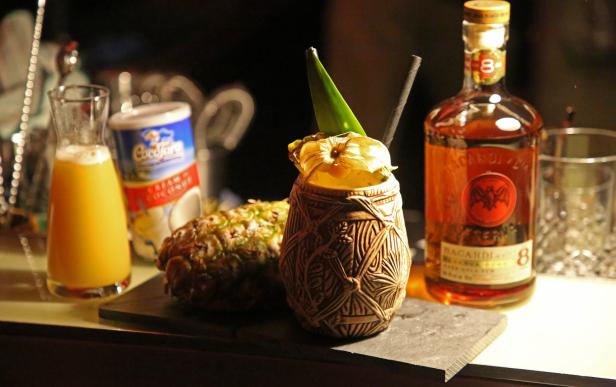 Ein Tiki-Cocktail mit Ananas, Saft und einer Flasche Bacardi Rum auf einer Bar.